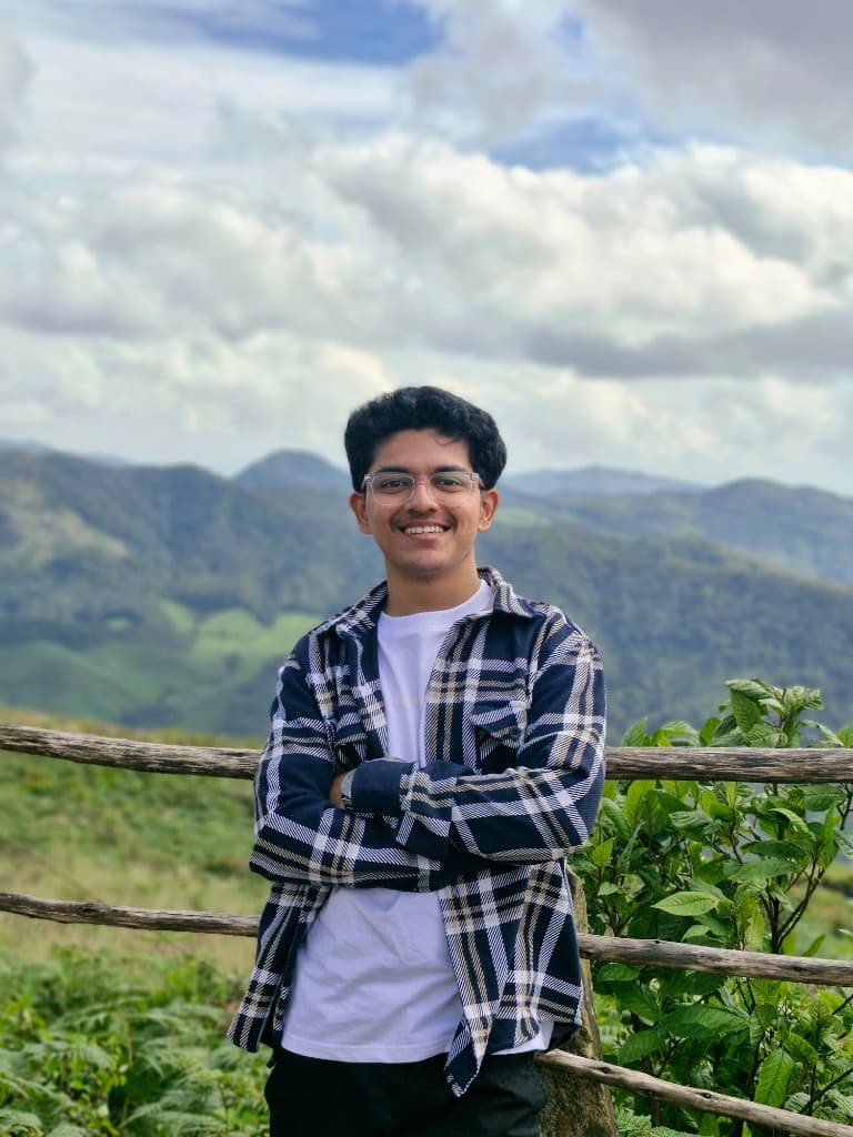 Vishwesh Shinde smiling with his arms crossed, wearing a plaid shirt over a white tee