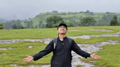 Vishwesh standing in a green meadow with his arms spread wide, looking up at the sky