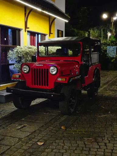 A red open-top jeep parked on a cobblestone street at night