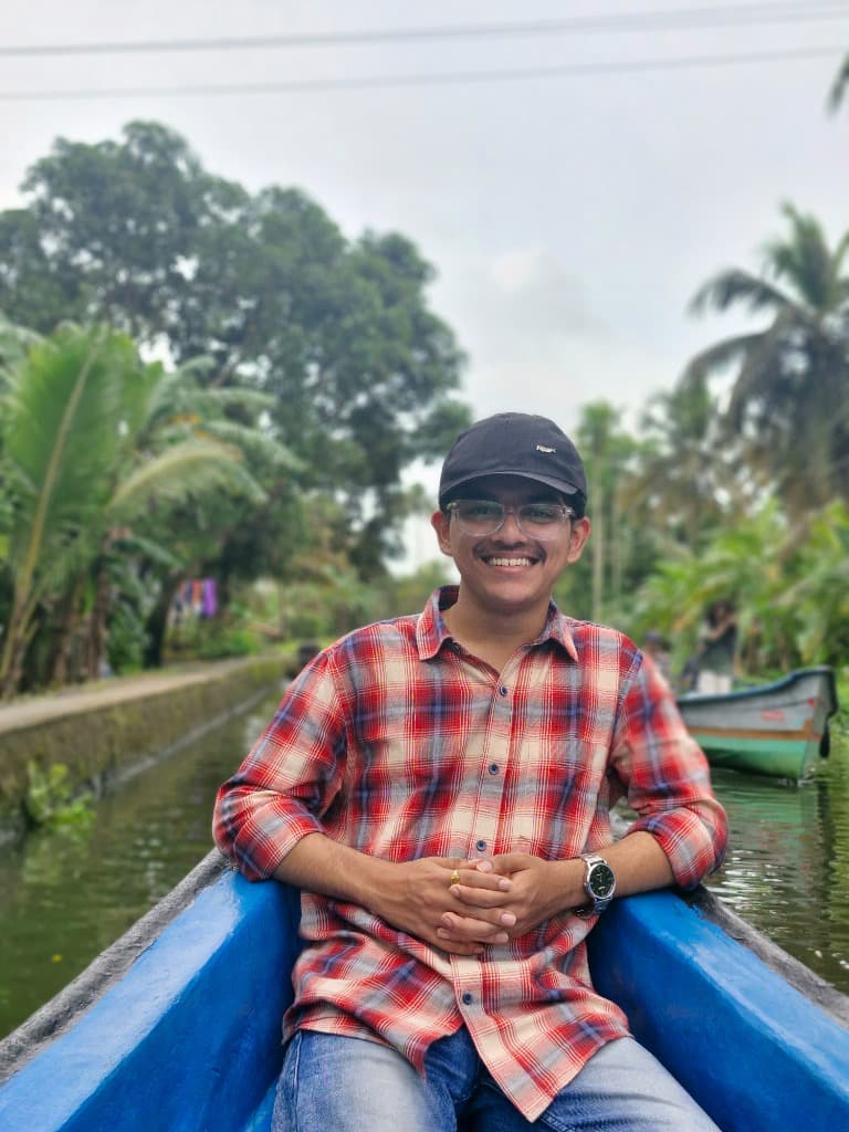 Vishwesh smiling while sitting in a blue boat in backwaters surrounded by palm trees